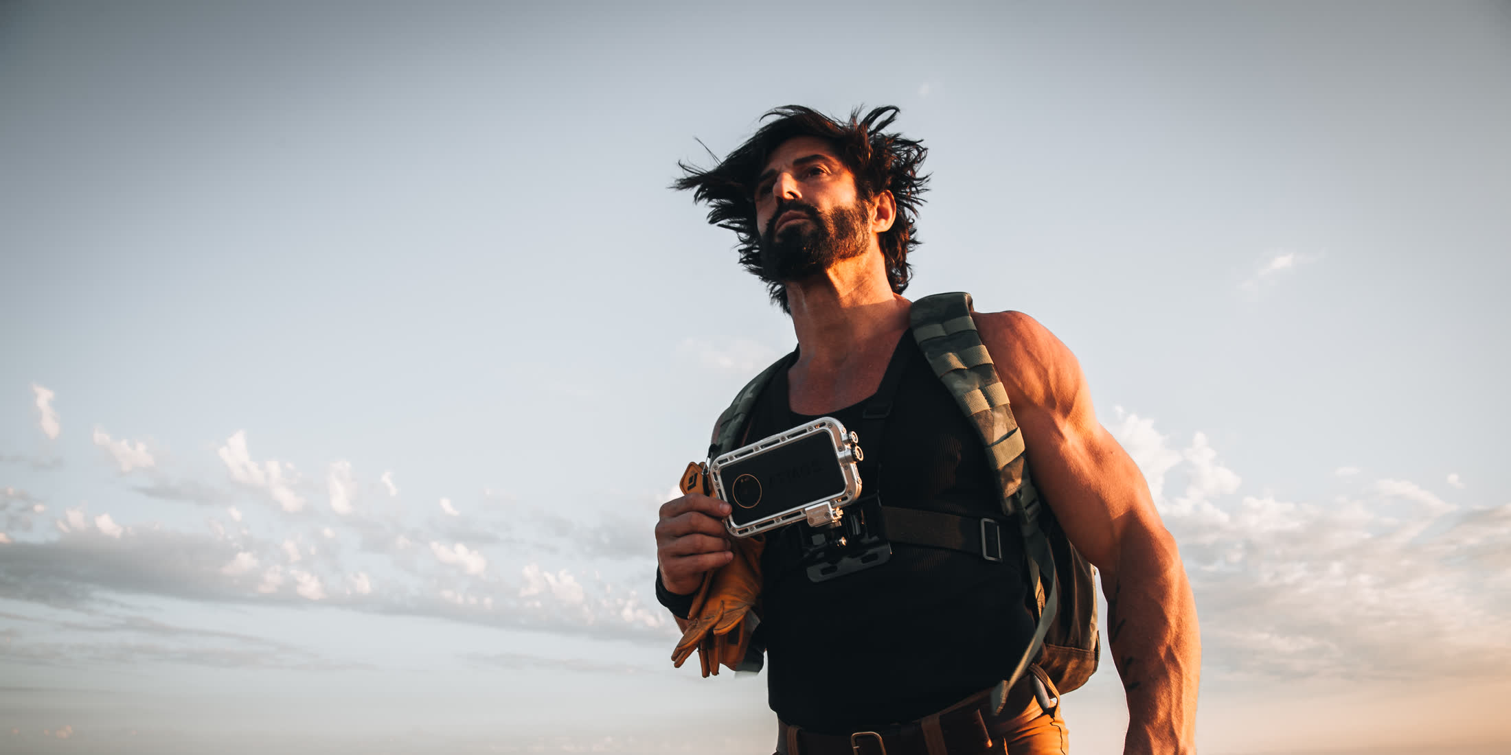 Man on a summit at dusk holding the Atmos cased phone against an open sky